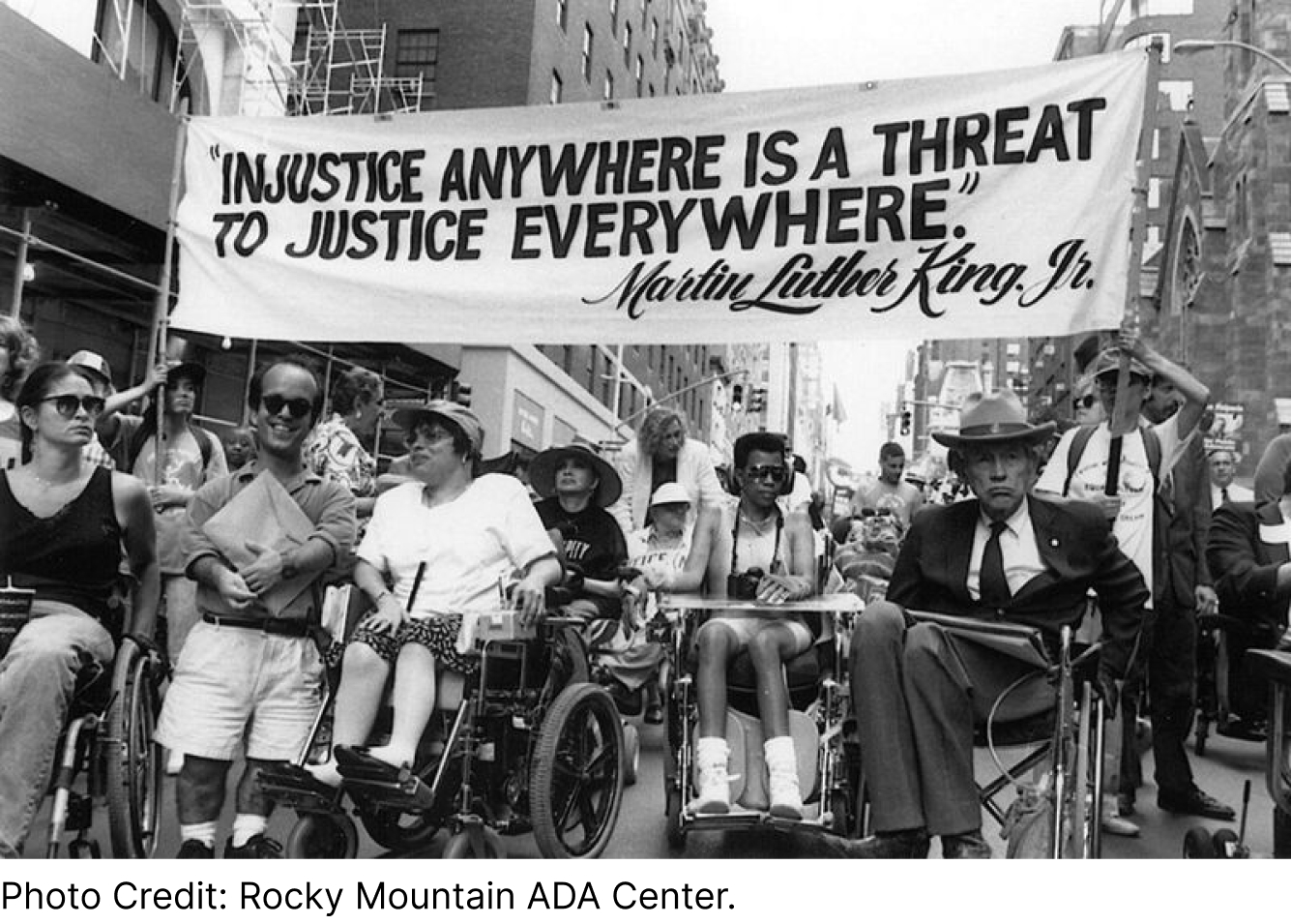 People marching in the streets holding a banner that reads 'Injustice anywhere is a threat to justice everywhere. Martin Luther King. Jr.' Photo credit in the image saying: 'Photo credit: Rocky Mountain ADA Center'